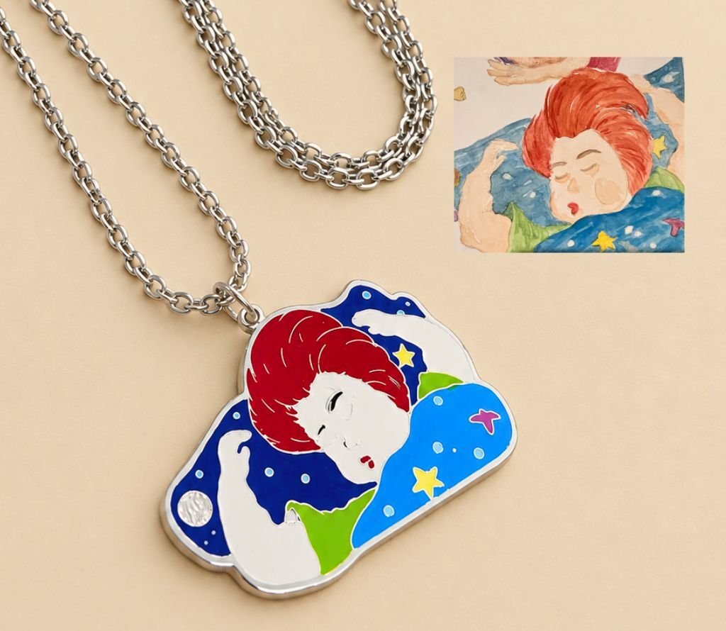Close-up of the sleeping child pendant beside the original drawing it was traced from